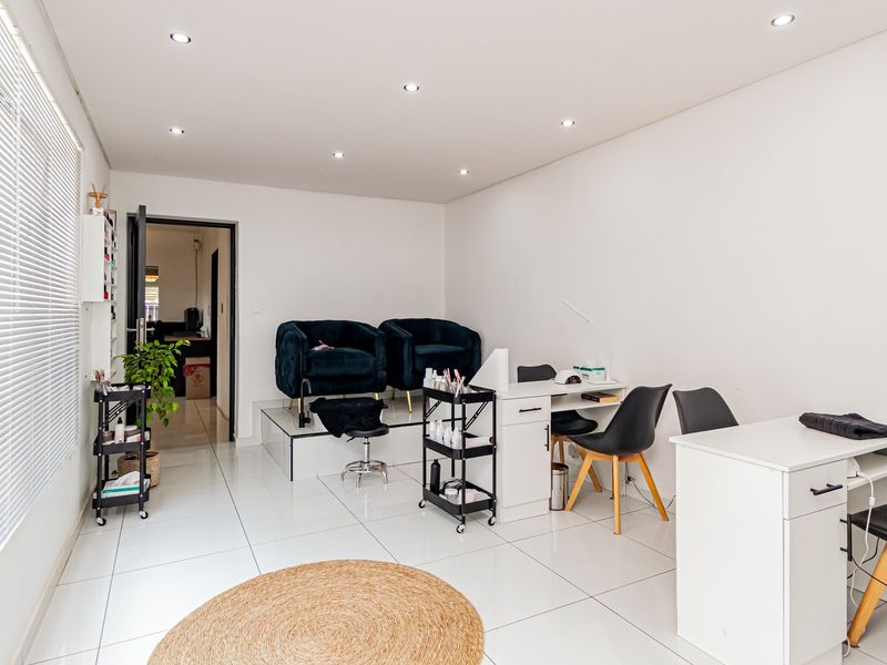 A bright, well-maintained utility space featuring tiled flooring, recessed downlighting, and large windows with venetian blinds, currently utilized as a salon area.