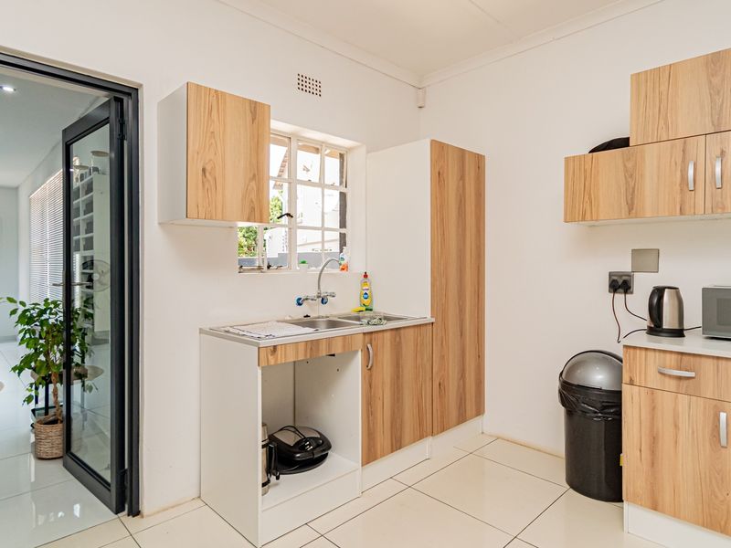 A functional scullery area featuring modern wood-look cabinetry, a stainless steel sink, and tiled flooring, providing additional prep and storage space.