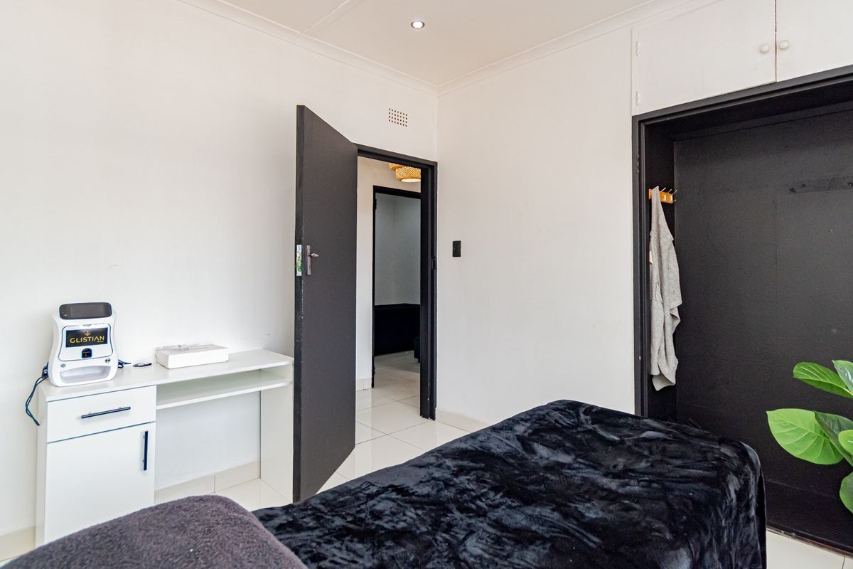 A clean bedroom featuring tiled flooring, recessed downlighting, and a built-in cupboard with a contrasting dark door frame.