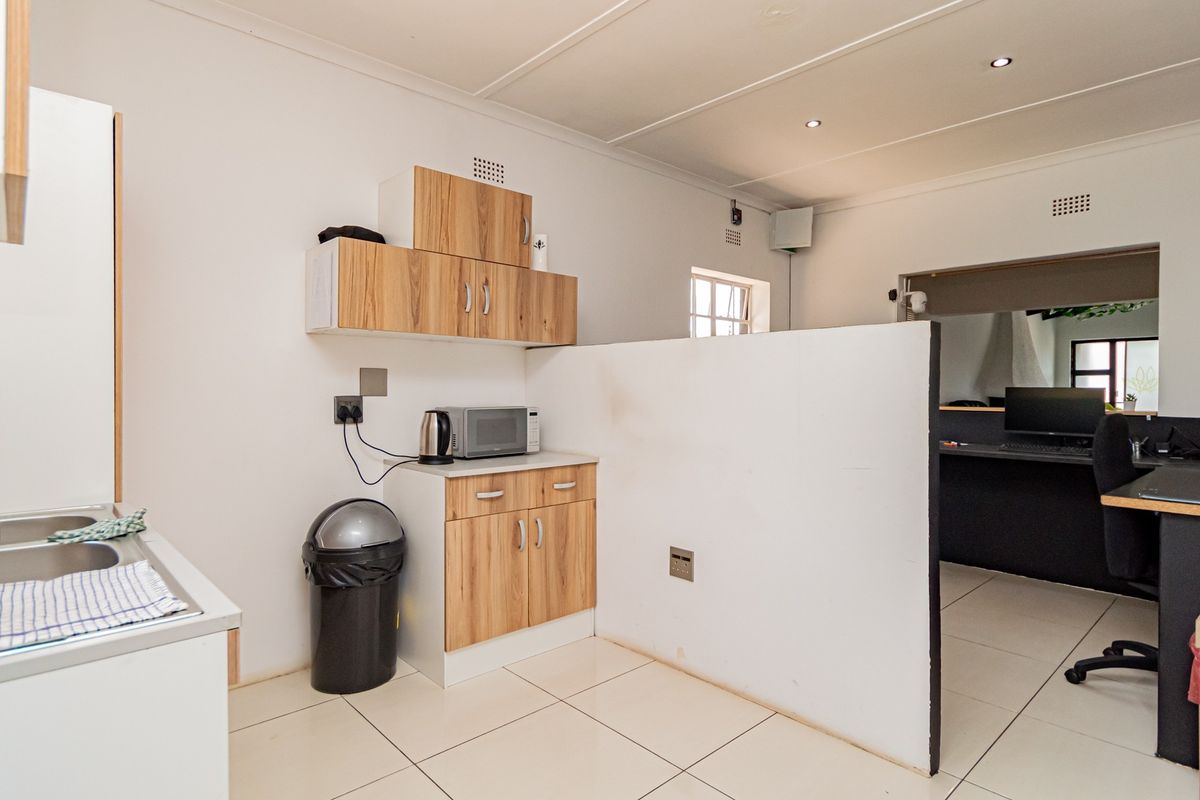 A functional kitchenette area featuring built-in wood-look cabinetry, a stainless steel sink, and tiled flooring, separated from an adjacent workspace by a partition wall.