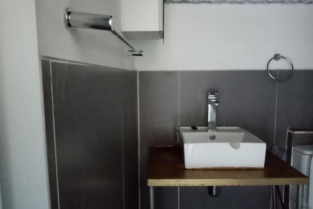 A compact bathroom featuring a modern vessel sink on a wooden vanity shelf with grey tiled splashbacks and chrome fixtures.