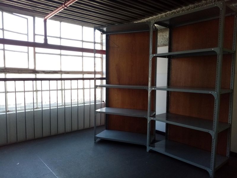 A functional utility space featuring industrial metal shelving, exposed ceiling, and large windows with metal safety railings.