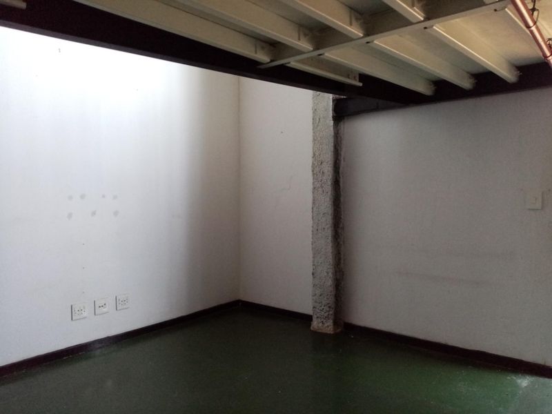 An empty, industrial-style room featuring exposed steel ceiling beams, a raw concrete pillar, and painted concrete flooring with multiple electrical power points.