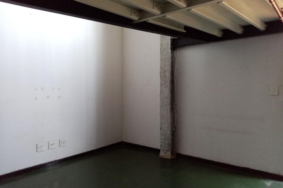 An empty, industrial-style room featuring exposed steel ceiling beams, a raw concrete pillar, and painted concrete flooring with multiple electrical power points.