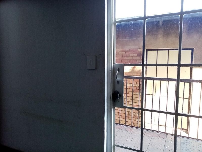 A view from inside looking out through a security gate onto a small balcony with metal railings and tiled flooring.