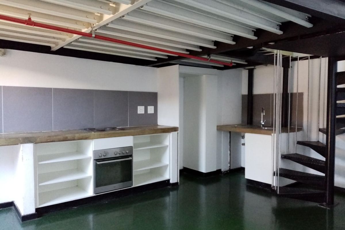 Industrial-style kitchen featuring exposed ceiling beams, a spiral staircase, built-in oven, electric hob, and concrete countertops in an open-plan layout.