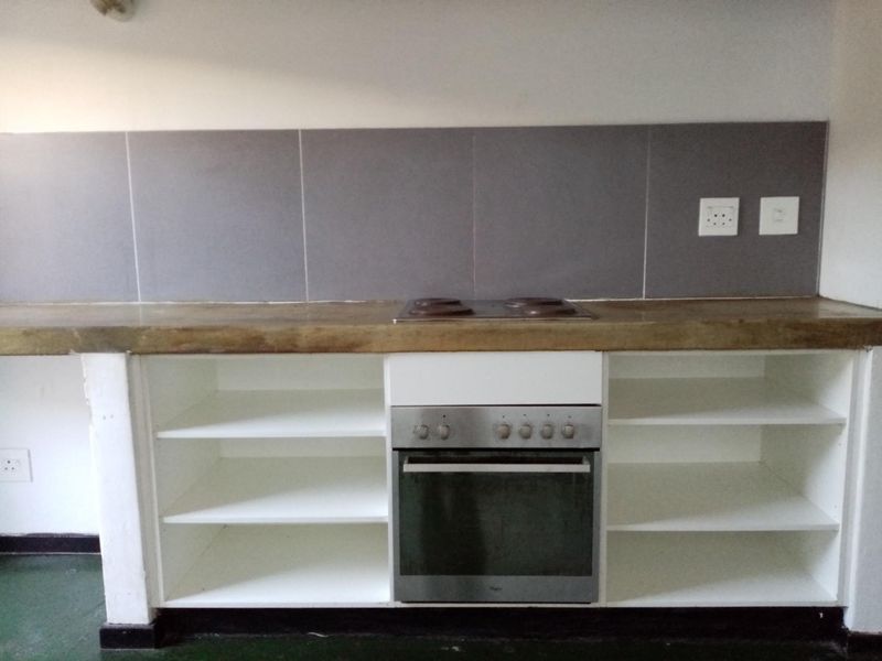 A functional kitchen area featuring an integrated oven, electric hob, concrete countertop, and open shelving with a grey tiled backsplash.