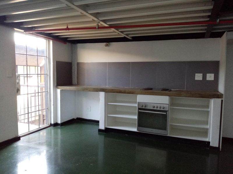 Industrial-style kitchen featuring an exposed ceiling, concrete countertop, built-in oven, and open shelving, with direct access to an outdoor area.