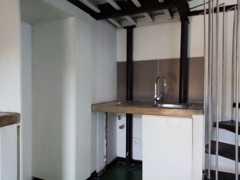 A compact kitchen area featuring a stainless steel sink, metal splashback, and adjacent spiral staircase, currently in need of renovation and finishing.