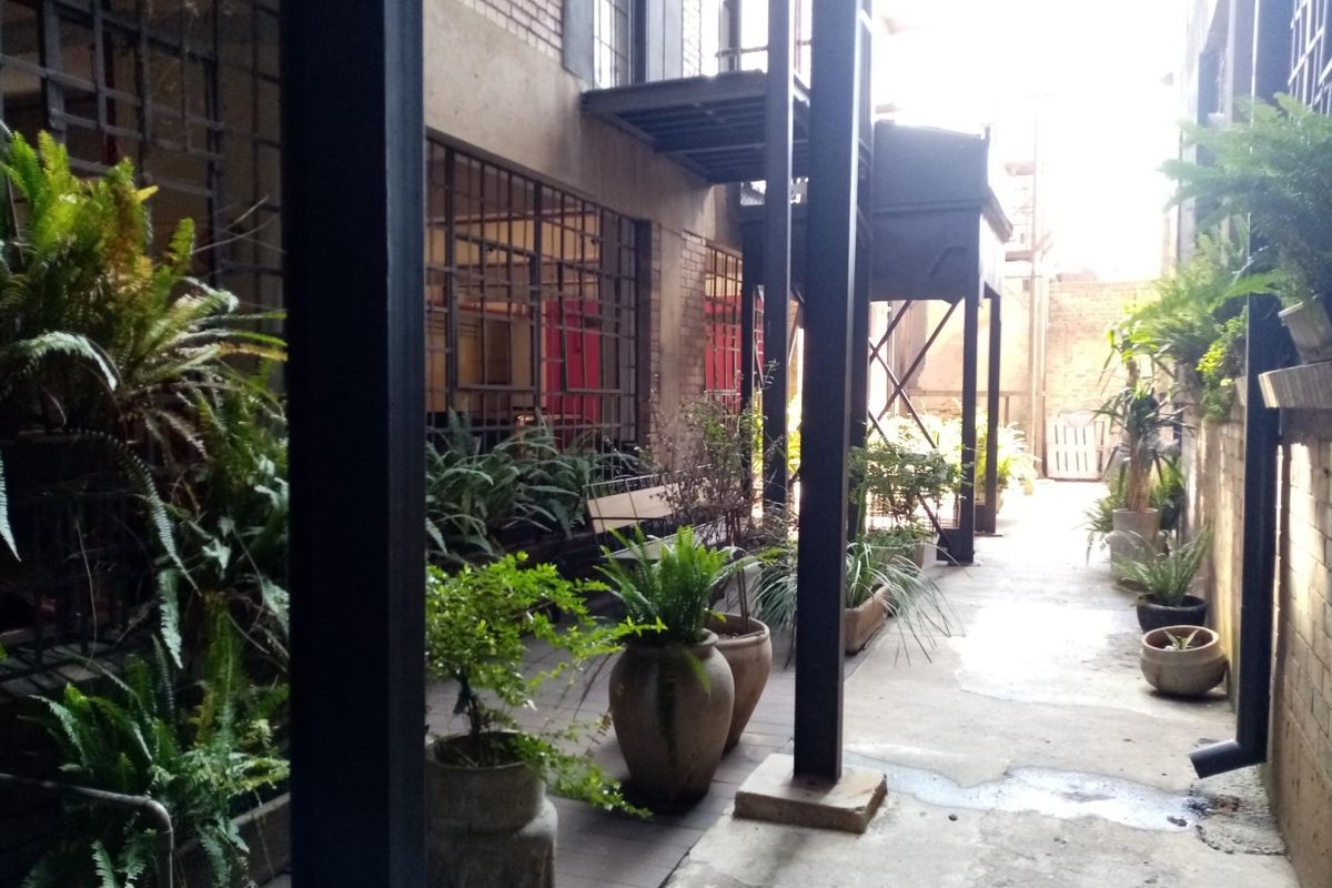 A rear exterior walkway featuring industrial-style steel columns, metal-framed windows, and a concrete path, offering a unique urban aesthetic.