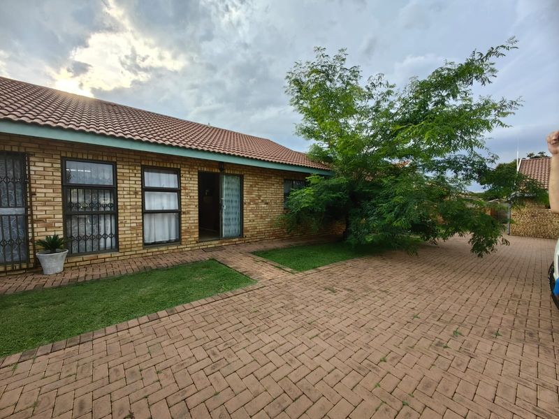 A front exterior view of a face brick townhouse featuring a tiled roof, paved driveway, and secure sliding door entrance.