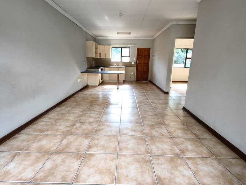 An empty open-plan living and kitchen area featuring tiled flooring, neutral walls, and functional built-in cabinetry with a breakfast counter.