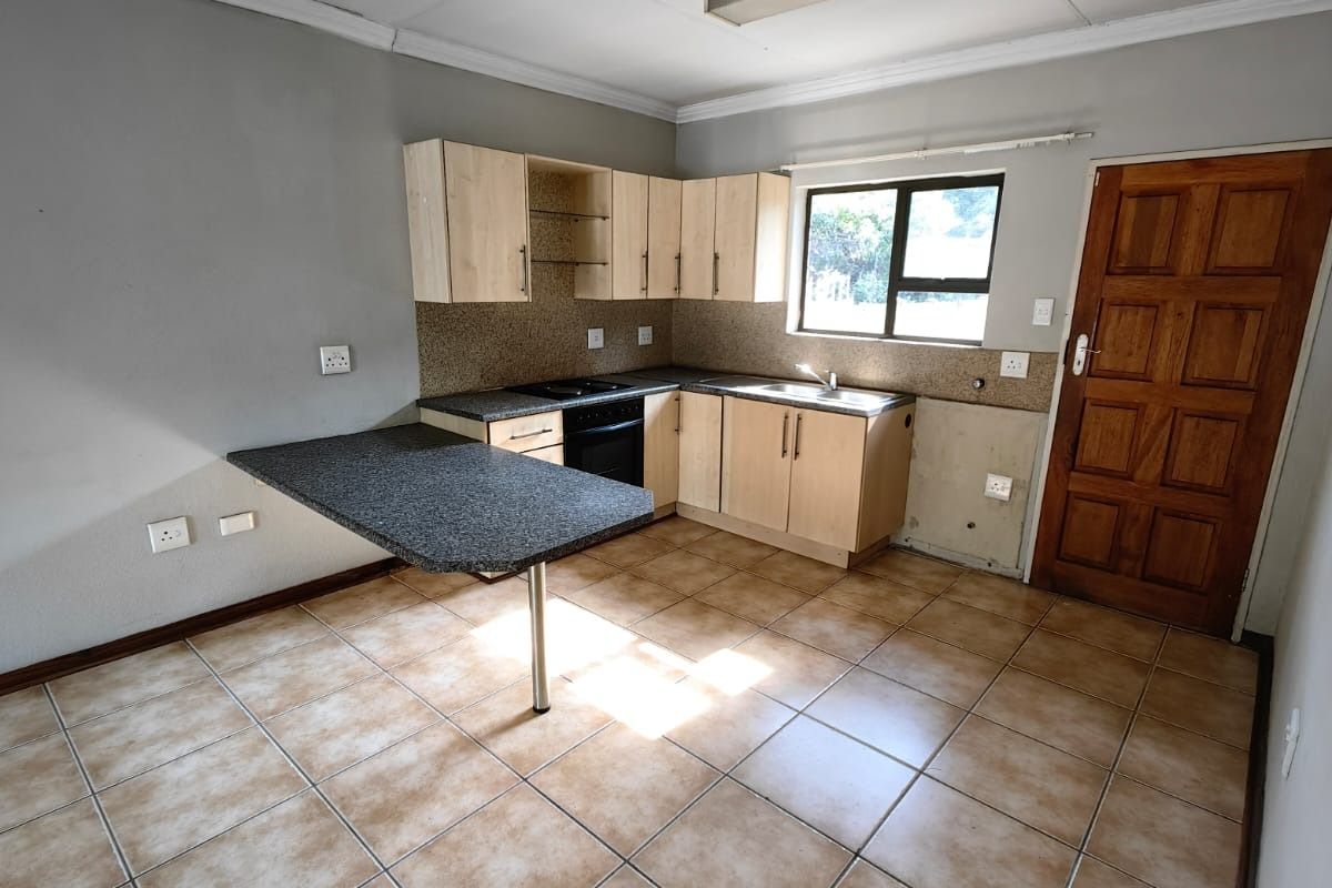 An empty kitchen featuring light wood cabinetry, a breakfast bar, integrated oven and hob, and ceramic tiled flooring, requiring minor cosmetic finishing.