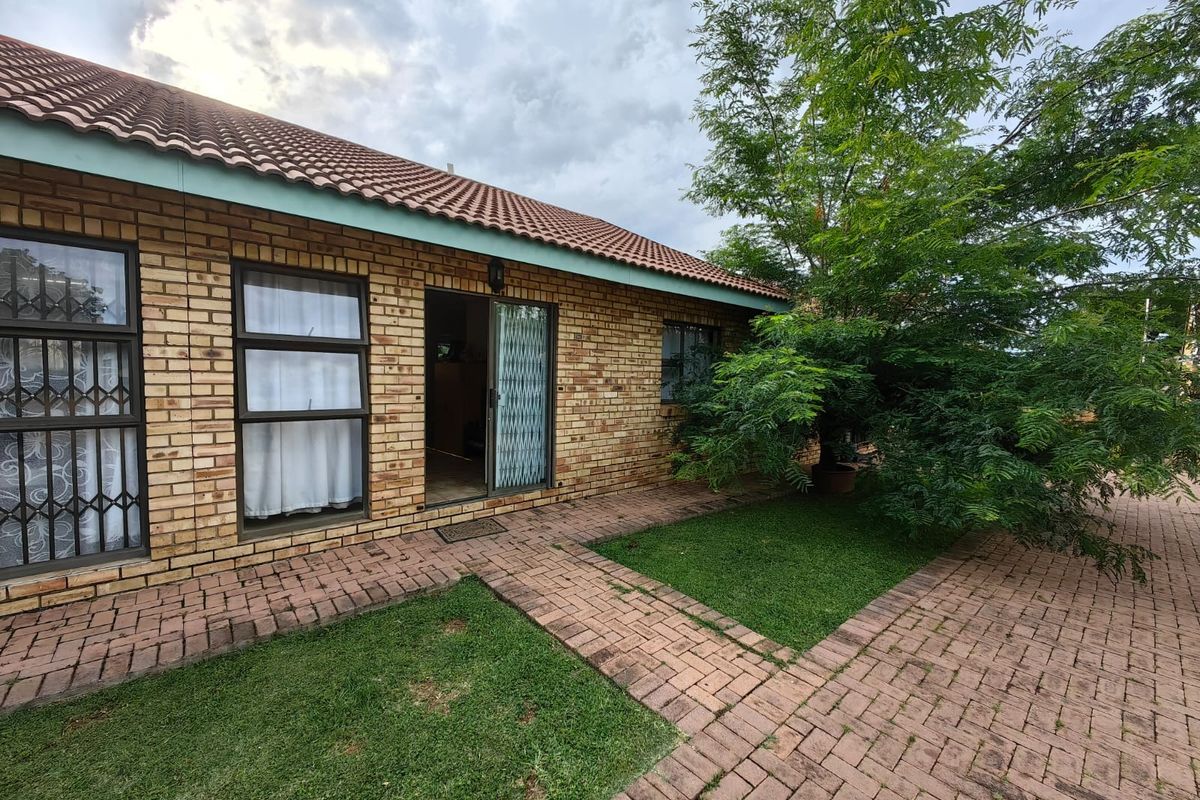 Rear exterior view of a face brick townhouse featuring a paved walkway, garden area, and sliding door access.