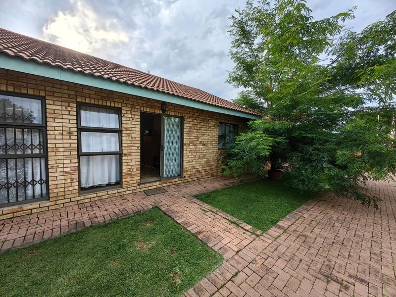 Rear exterior view of a face brick townhouse featuring a paved walkway, garden area, and sliding door access.