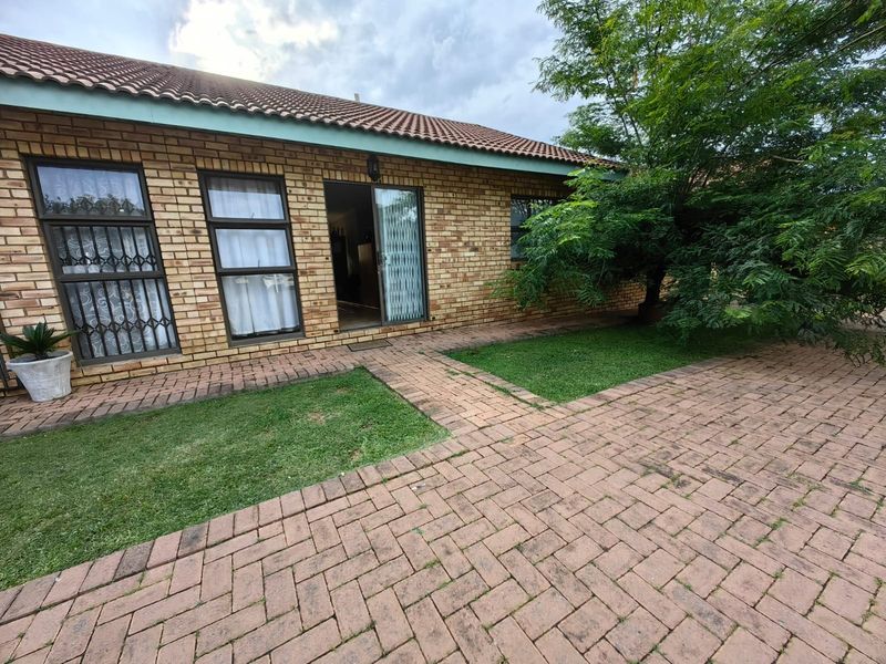 Rear exterior view of a townhouse featuring a brick facade, tiled roof, paved patio area, and security gates leading into the home.