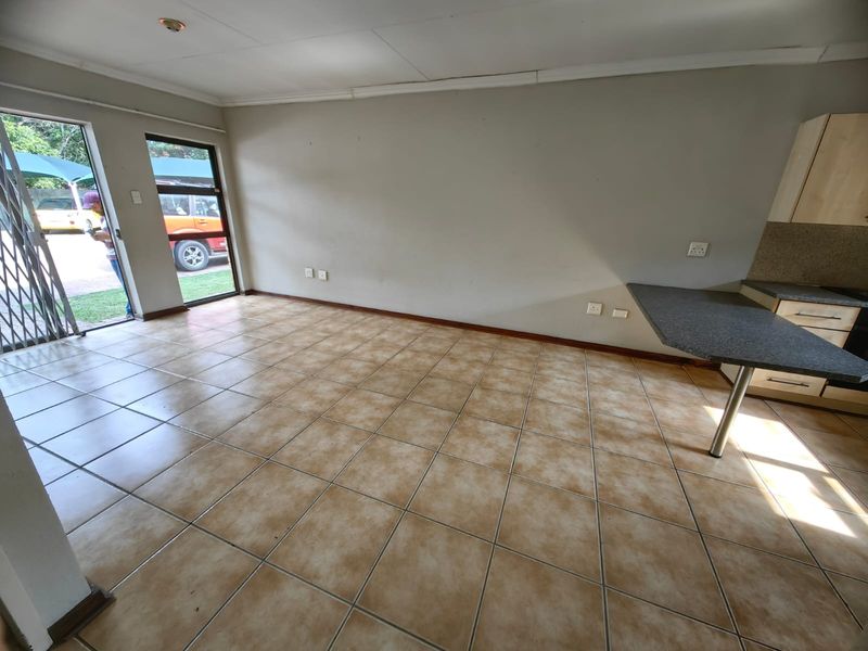 Open plan living area featuring ceramic tiled flooring, a compact kitchen corner with laminate countertops, and direct access to the exterior via a sliding door.