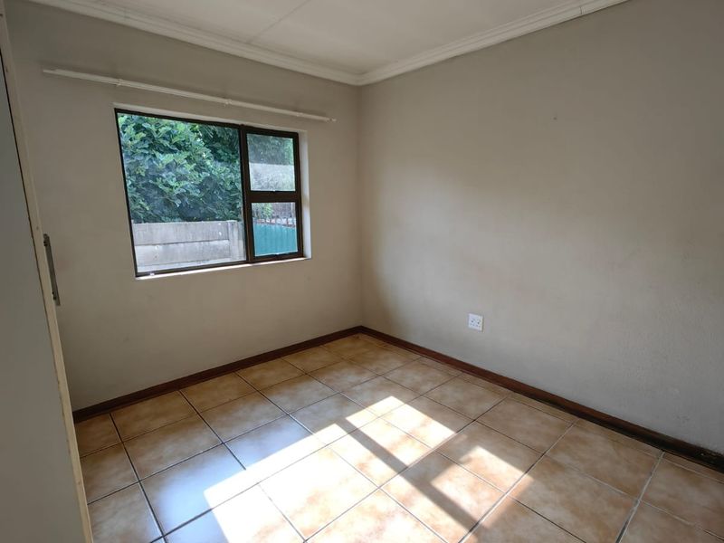 An empty bedroom featuring tiled flooring, neutral walls, and a window providing natural light, ready for personalization.