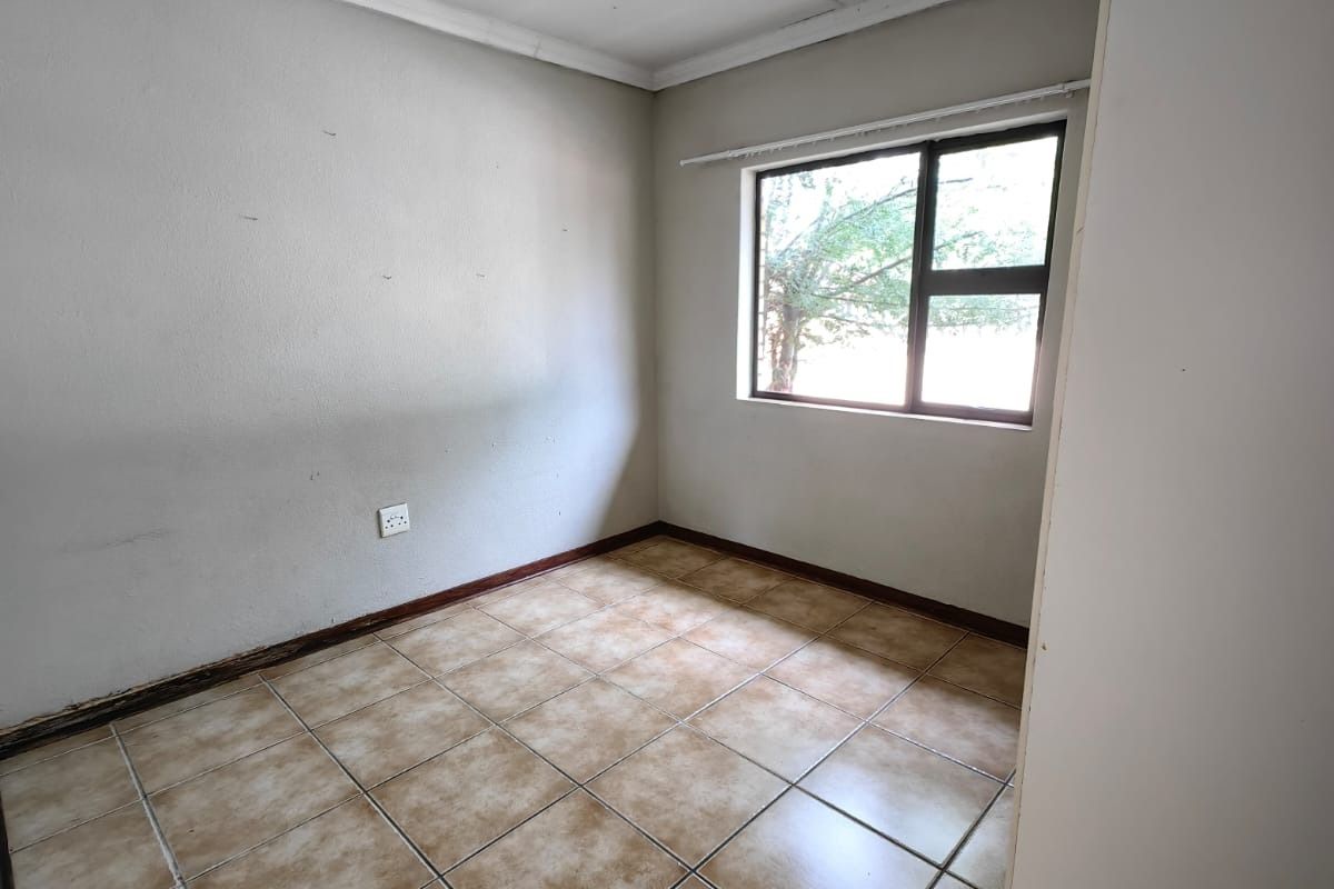 An empty bedroom featuring tiled flooring, coving, and a window, presenting a blank canvas ready for renovation or staging.