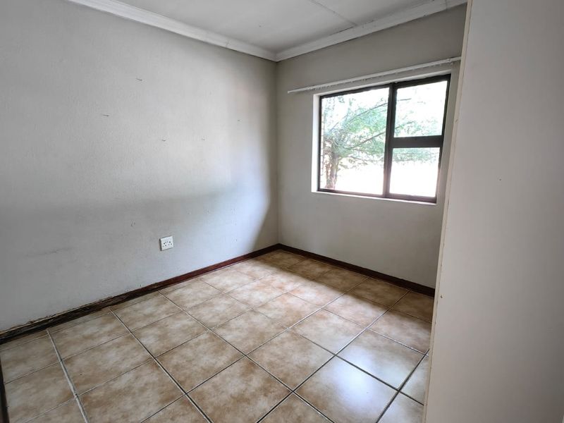 An empty bedroom featuring tiled flooring, coving, and a window, presenting a blank canvas ready for renovation or staging.