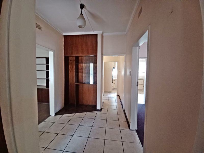 A central hallway featuring tiled flooring and a built-in wooden display cabinet, providing access to multiple rooms within the home.