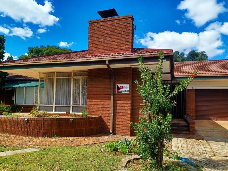 Front elevation of a single-story brick house featuring a prominent chimney, tiled roof, paved driveway, and an integrated garage.