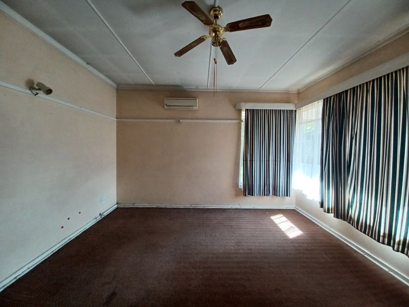 An empty living room featuring carpet flooring, a ceiling fan, and a wall-mounted air conditioning unit.
