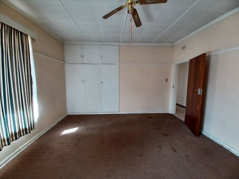 An empty bedroom featuring built-in cupboards, a ceiling fan, and carpeted flooring, offering a blank canvas for renovation or restyling.