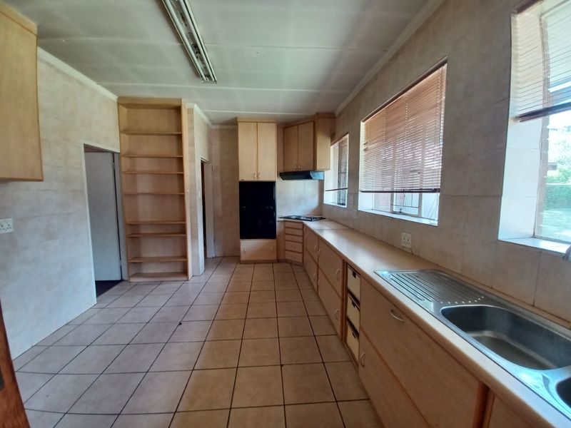 A spacious, empty kitchen featuring built-in cabinetry, a stainless steel sink, and integrated oven and hob, offering a blank canvas for renovation.