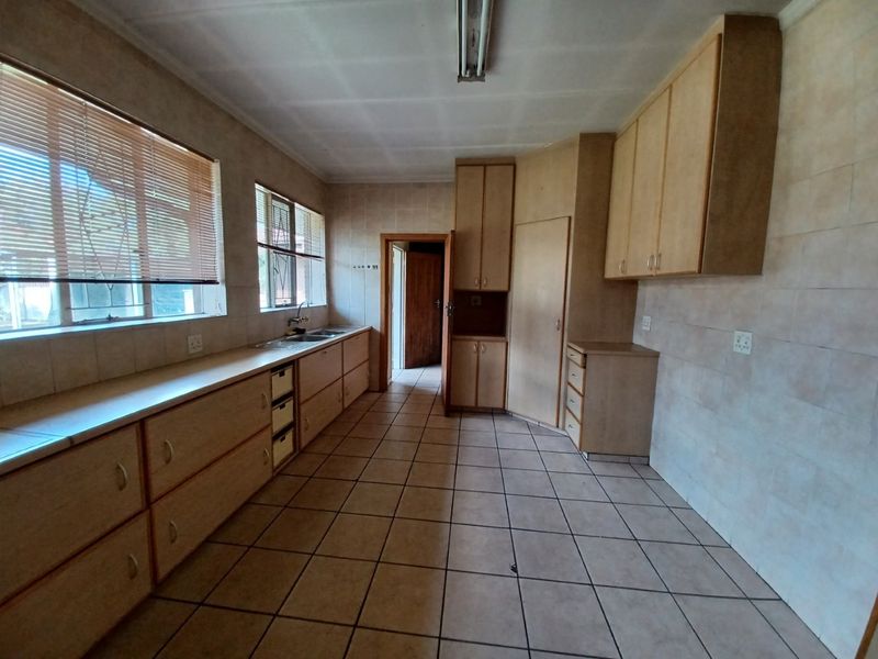 A spacious, empty kitchen featuring extensive built-in cabinetry, tiled walls, and tiled flooring, offering a blank canvas for a modern renovation.