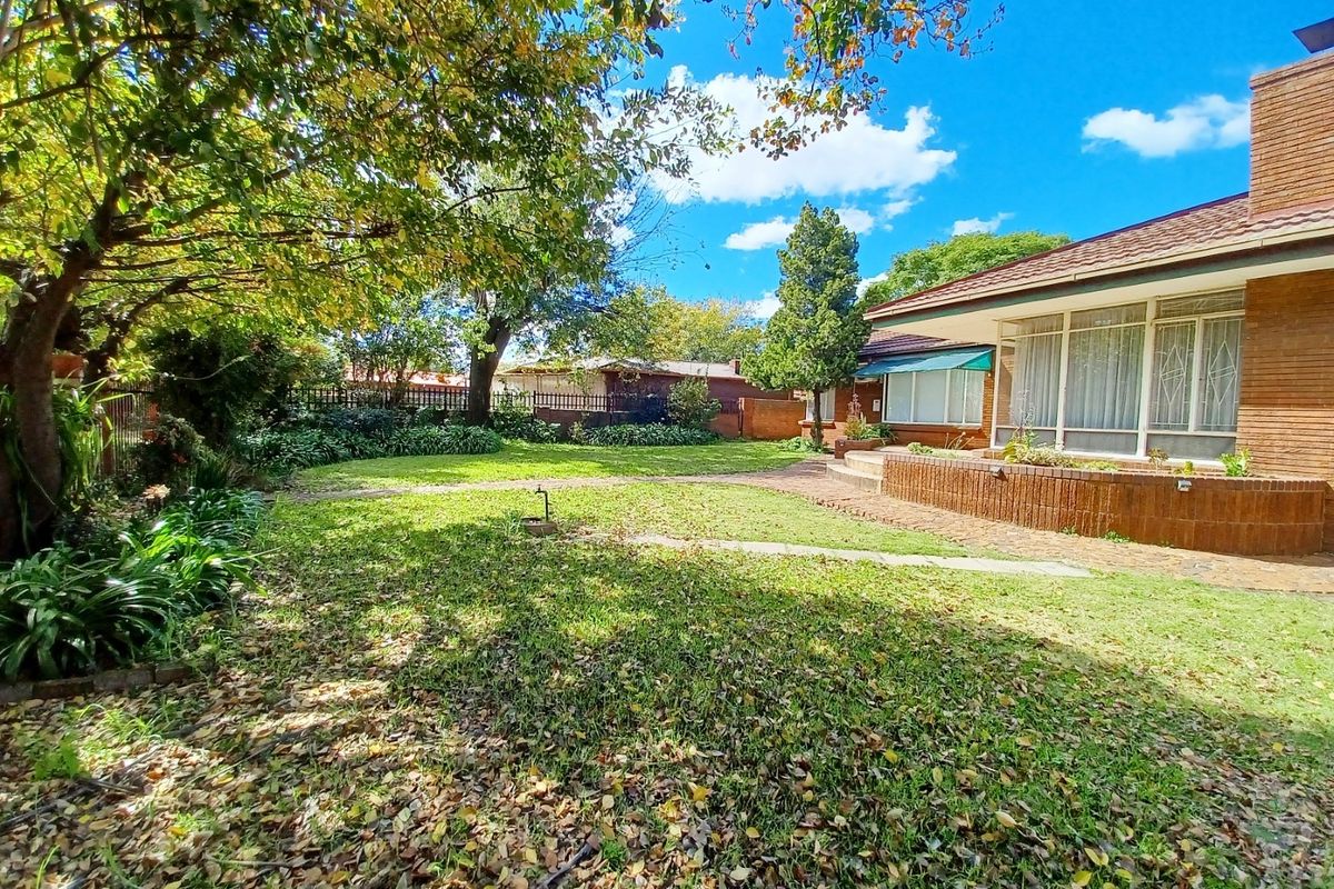 A spacious rear garden featuring a brick patio, established trees, and a brick-faced house exterior with a tiled roof.