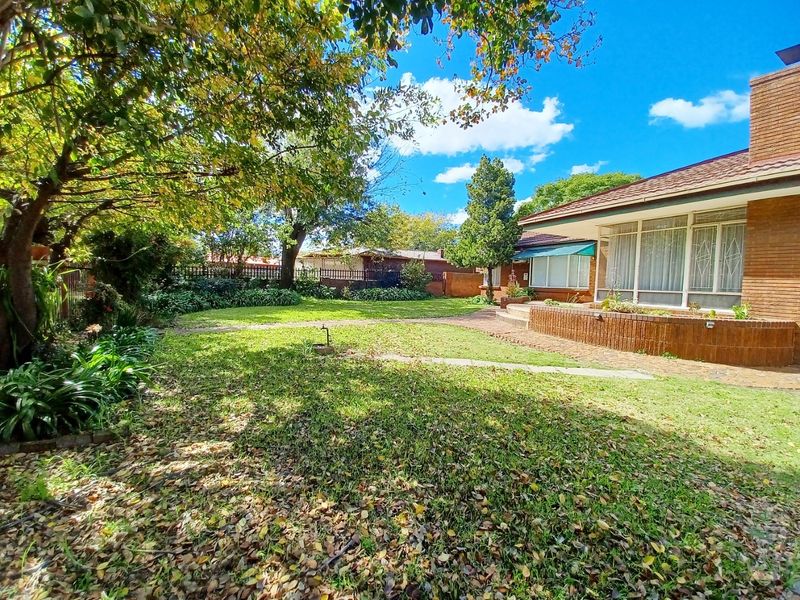 A spacious rear garden featuring a brick patio, established trees, and a brick-faced house exterior with a tiled roof.