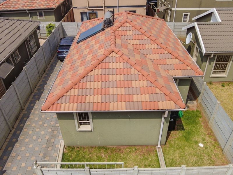 Aerial view of the property showing the tiled roof with solar water heating system, paved driveway, and surrounding precast concrete boundary walls.