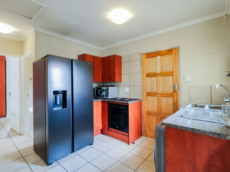 Functional kitchen featuring wood-finish cabinetry, laminate countertops, built-in oven and hob, tiled flooring, and a stainless steel sink.