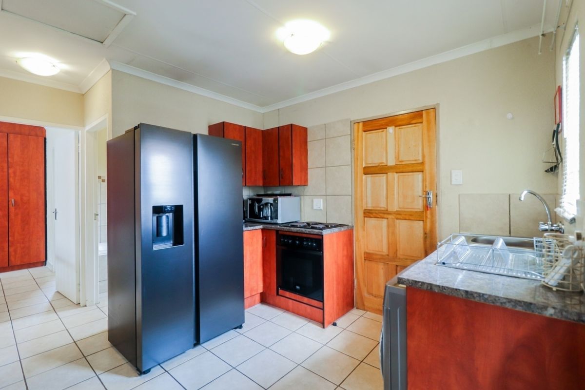 Functional kitchen featuring wood-finish cabinetry, laminate countertops, built-in oven and hob, tiled flooring, and a stainless steel sink.