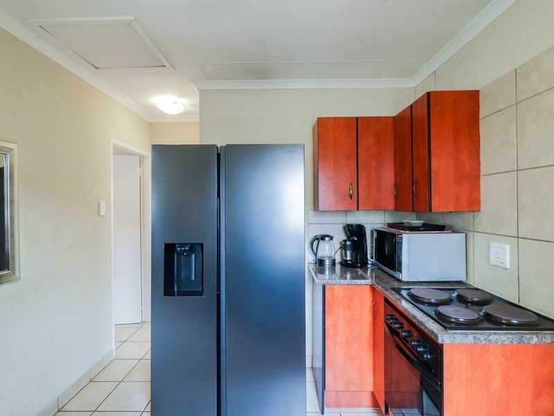 Compact kitchen featuring wood-finish cabinetry, tiled backsplash, electric hob, and built-in oven, with tiled flooring throughout.