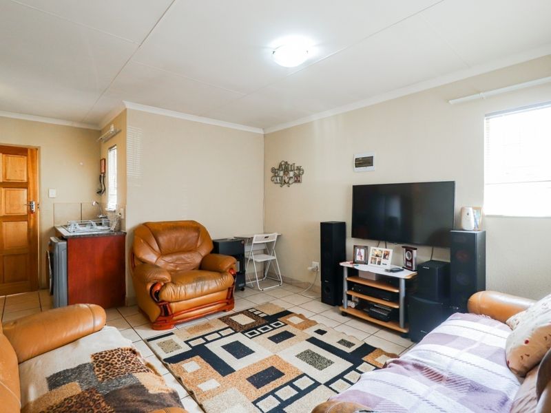Open-plan living area featuring tiled flooring and a compact kitchenette with built-in cabinetry and sink.