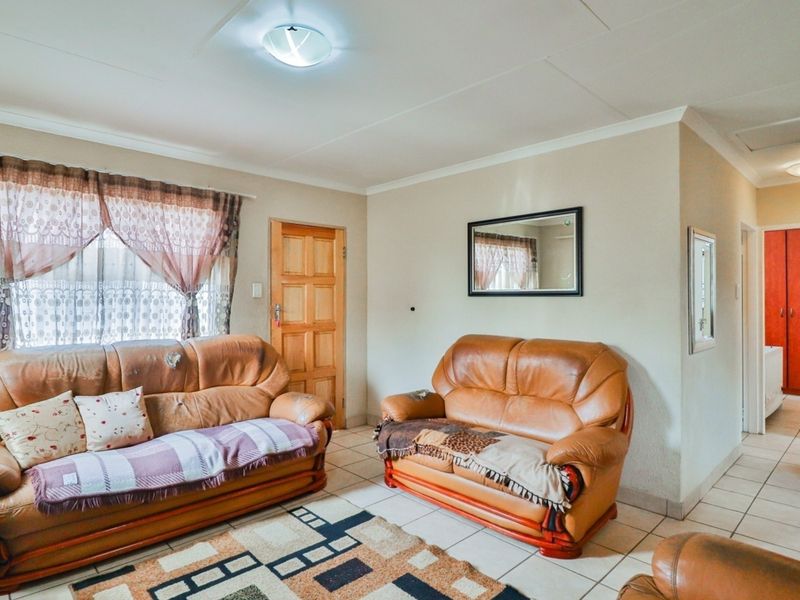A living room featuring tiled flooring, a wooden entrance door, and built-in storage cupboards, offering a functional space with potential for cosmetic updates.