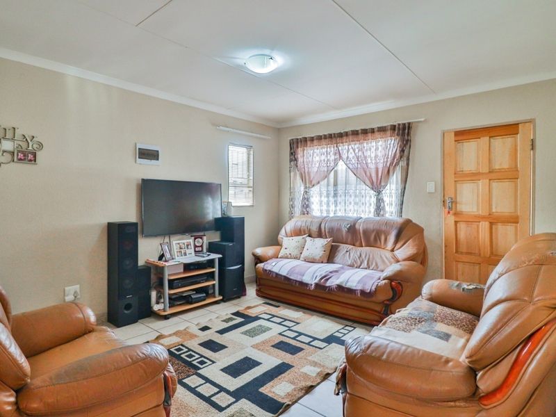 A functional living room featuring tiled flooring, a timber panel door, and neutral wall finishes, providing a comfortable and practical space for relaxation.