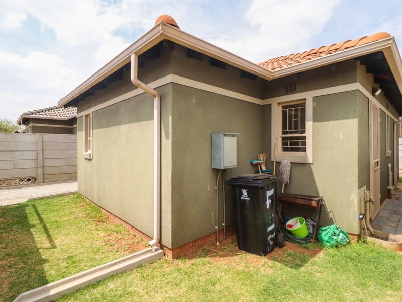 Rear exterior view of the property featuring a tiled roof, guttering, security bars on windows, and a paved walkway alongside a small garden area.