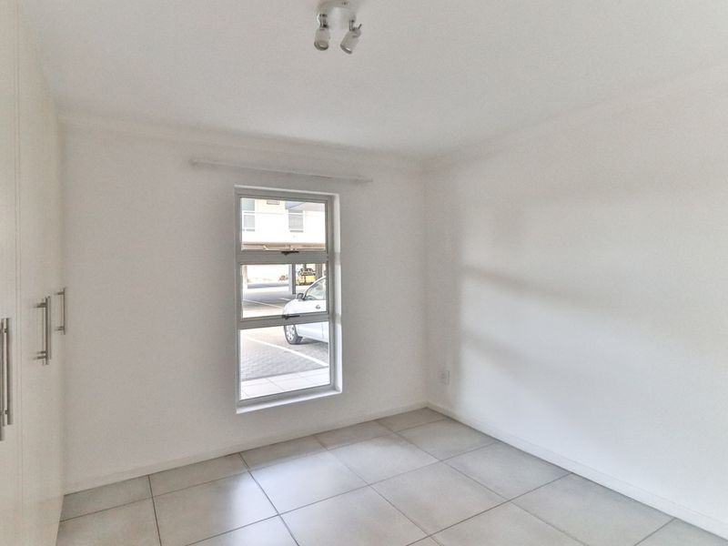 A clean, empty bedroom featuring neutral tiled flooring, built-in cupboards, and a window providing natural light.