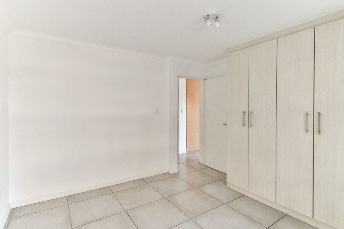 A bright, empty bedroom featuring neutral tiled flooring and ample built-in cupboard storage, offering a clean and versatile space.
