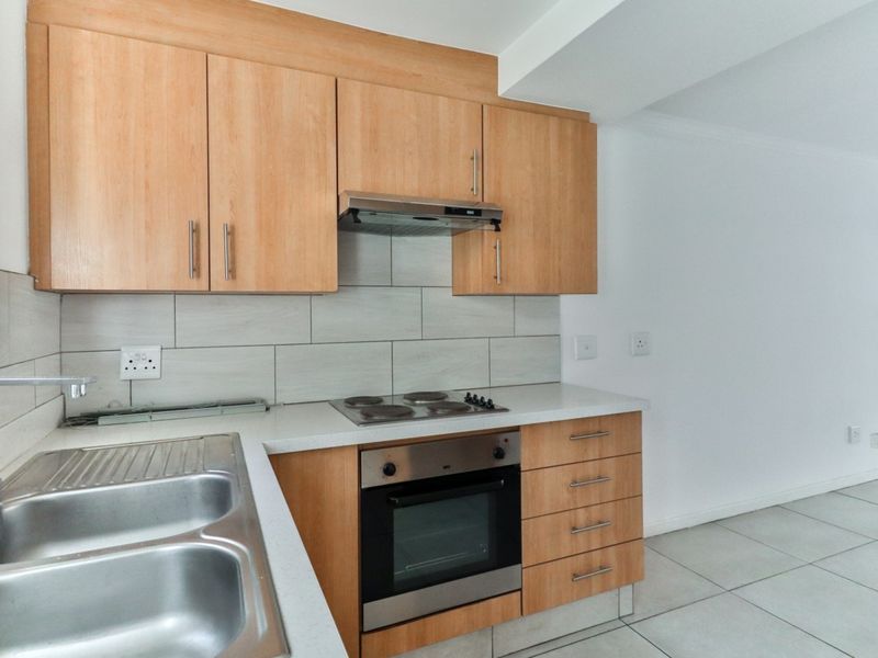 A clean, modern kitchen featuring light wood cabinetry, built-in oven, electric hob, extractor fan, and a double stainless steel sink with tiled backsplash.