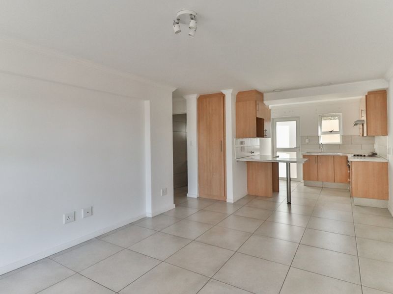 An open-plan living and kitchen area featuring neutral tiled flooring, light wood cabinetry, and a functional breakfast bar layout.