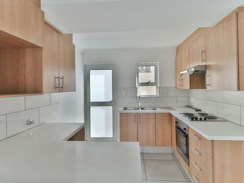 A functional kitchen featuring light wood cabinetry, stone countertops, a built-in oven, electric hob, and tiled backsplash with direct access to an exterior door.