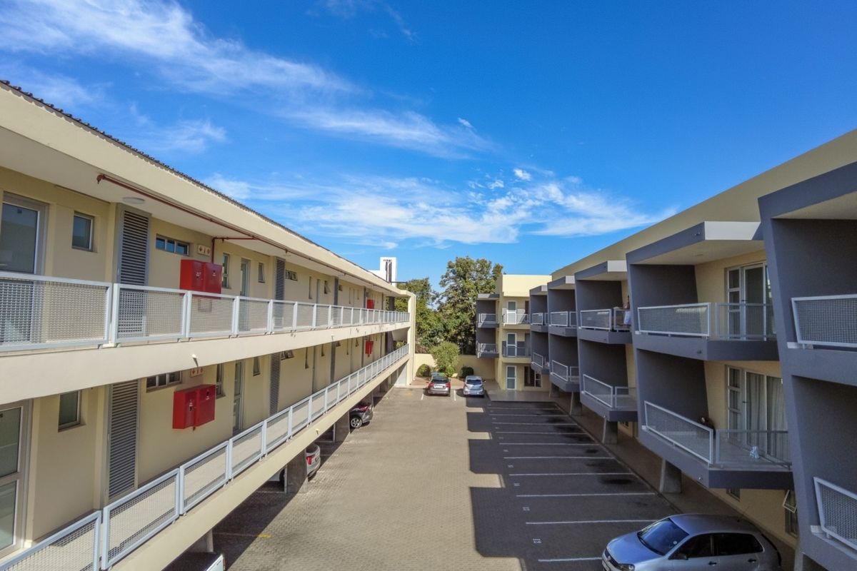 An elevated view of an apartment complex courtyard featuring paved parking bays, multi-level balconies with metal railings, and external building access.