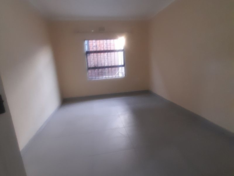 A vacant bedroom featuring neutral wall paint, tiled flooring, and a window fitted with security bars.