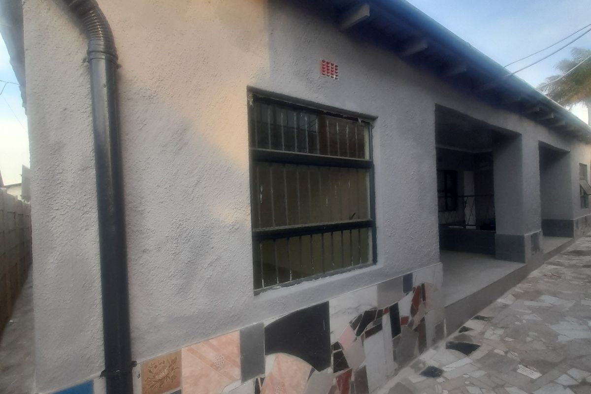 Rear exterior view of the cottage featuring a textured facade with decorative tile base, exposed roof rafters, and a paved outdoor area.