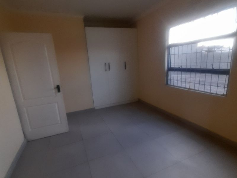 A clean, empty bedroom featuring tiled flooring, a built-in wardrobe, and a window fitted with security bars.