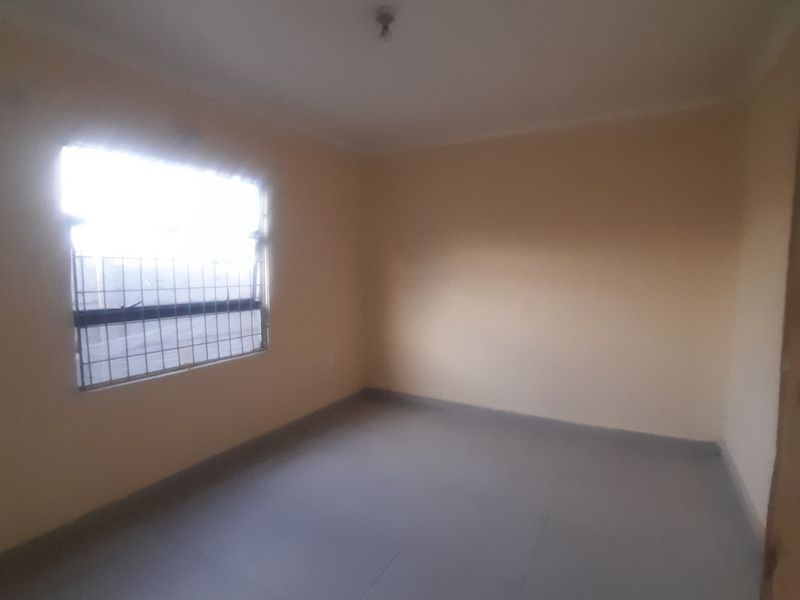 An empty bedroom featuring tiled flooring, neutral walls, and a window fitted with security bars.